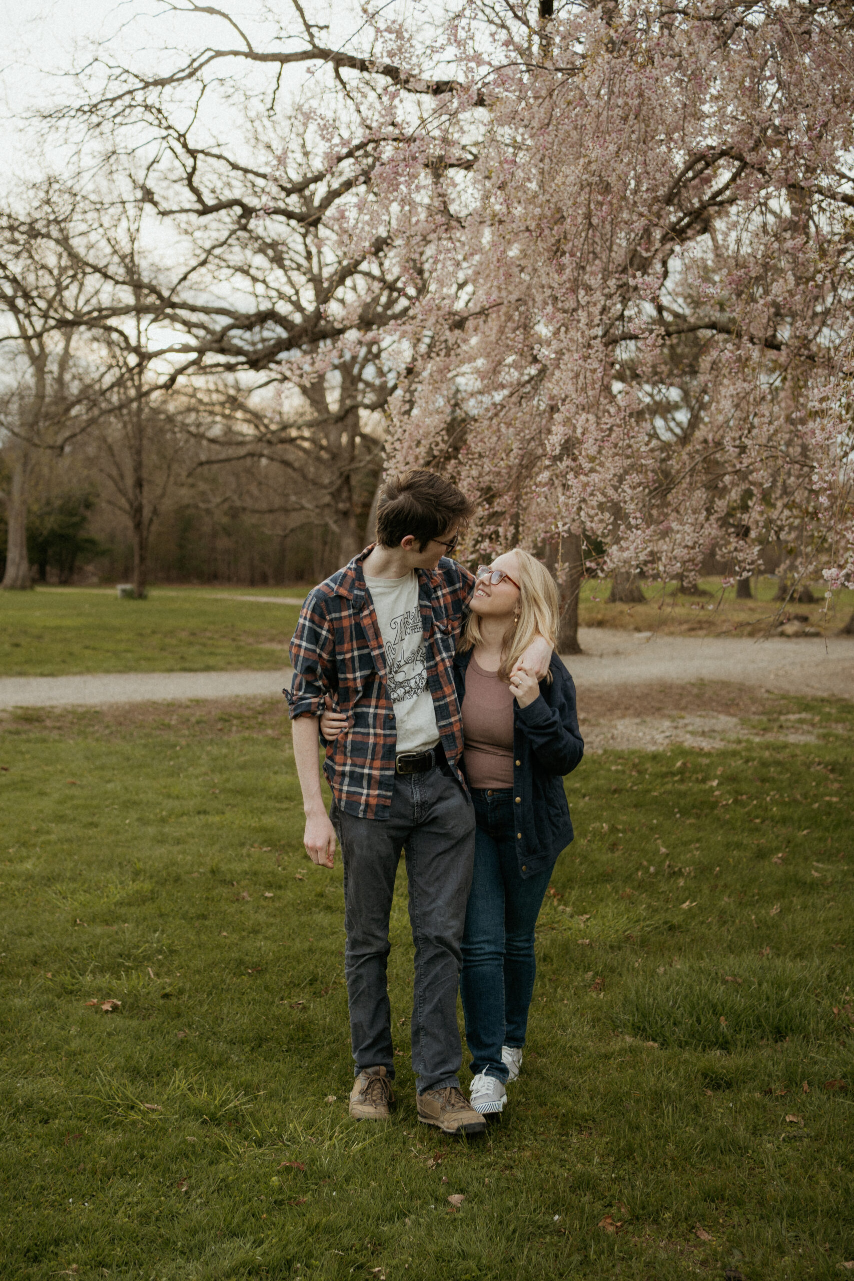 Engaged couple walks side by side, exchanging affectionate glances and smiles during their spring engagement photo session at Borderland State Park in Easton, MA