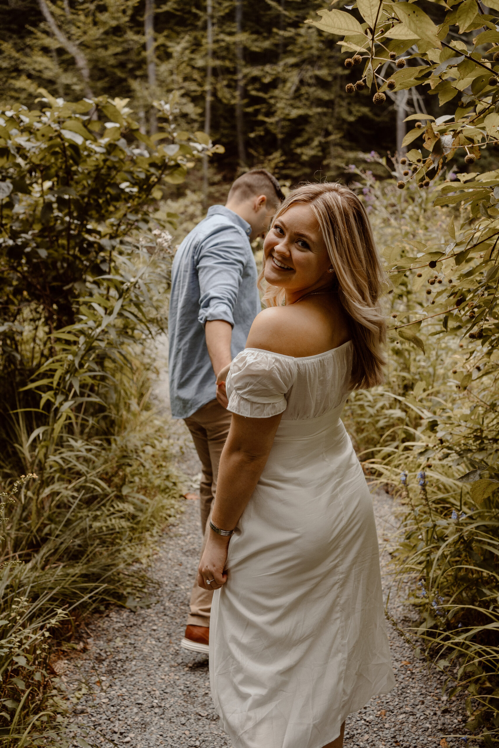 Hand in hand, a couple explores a woodland path, their laughter echoing through the Garden in The Woods in Framingham, MA during their engagement photo session.
