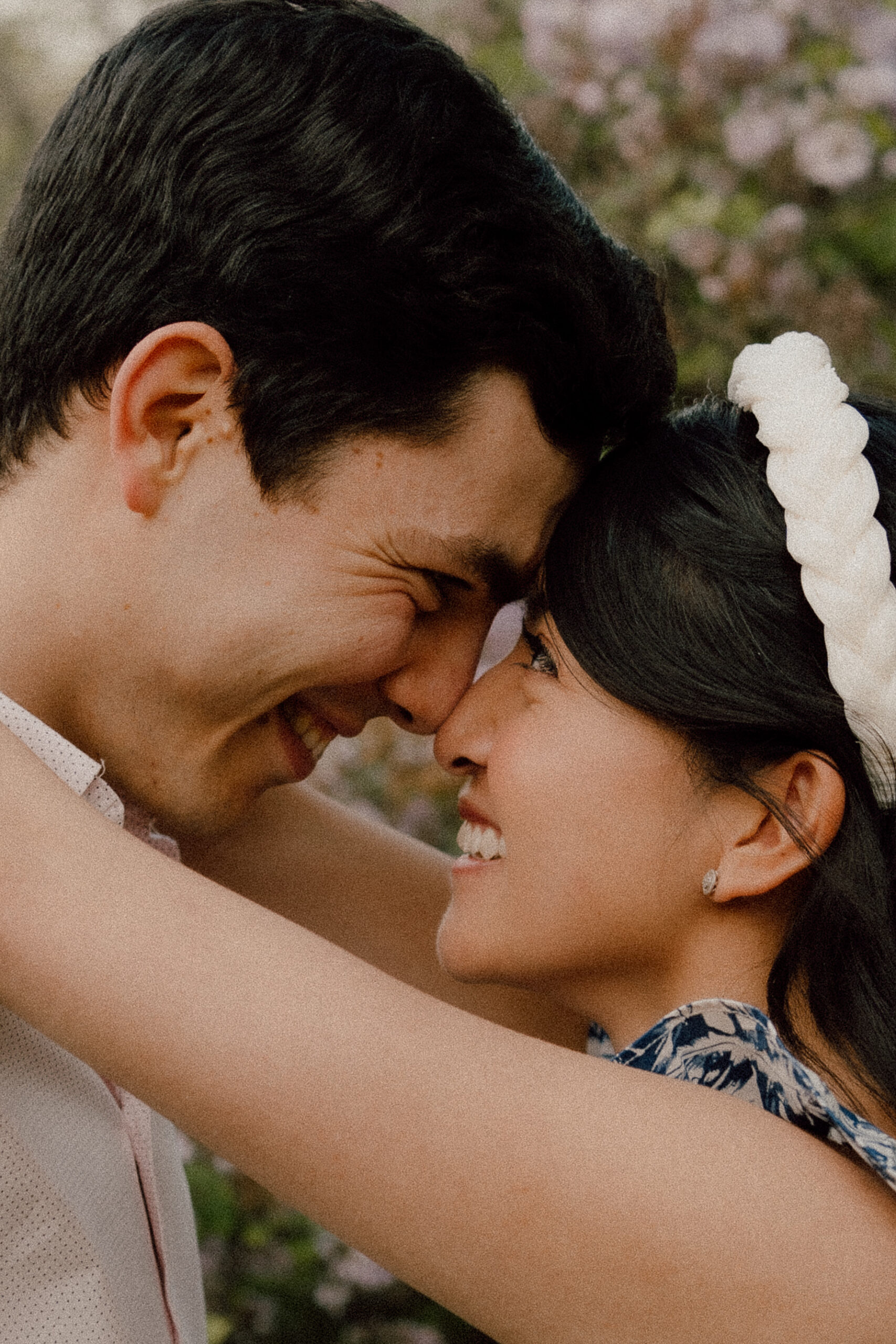 Engaged couple shares an intimate moment, pressing foreheads and gazing into each other's eyes amidst blooming lilac trees during their spring engagement session at the Arnold Arboretum in Boston, MA.