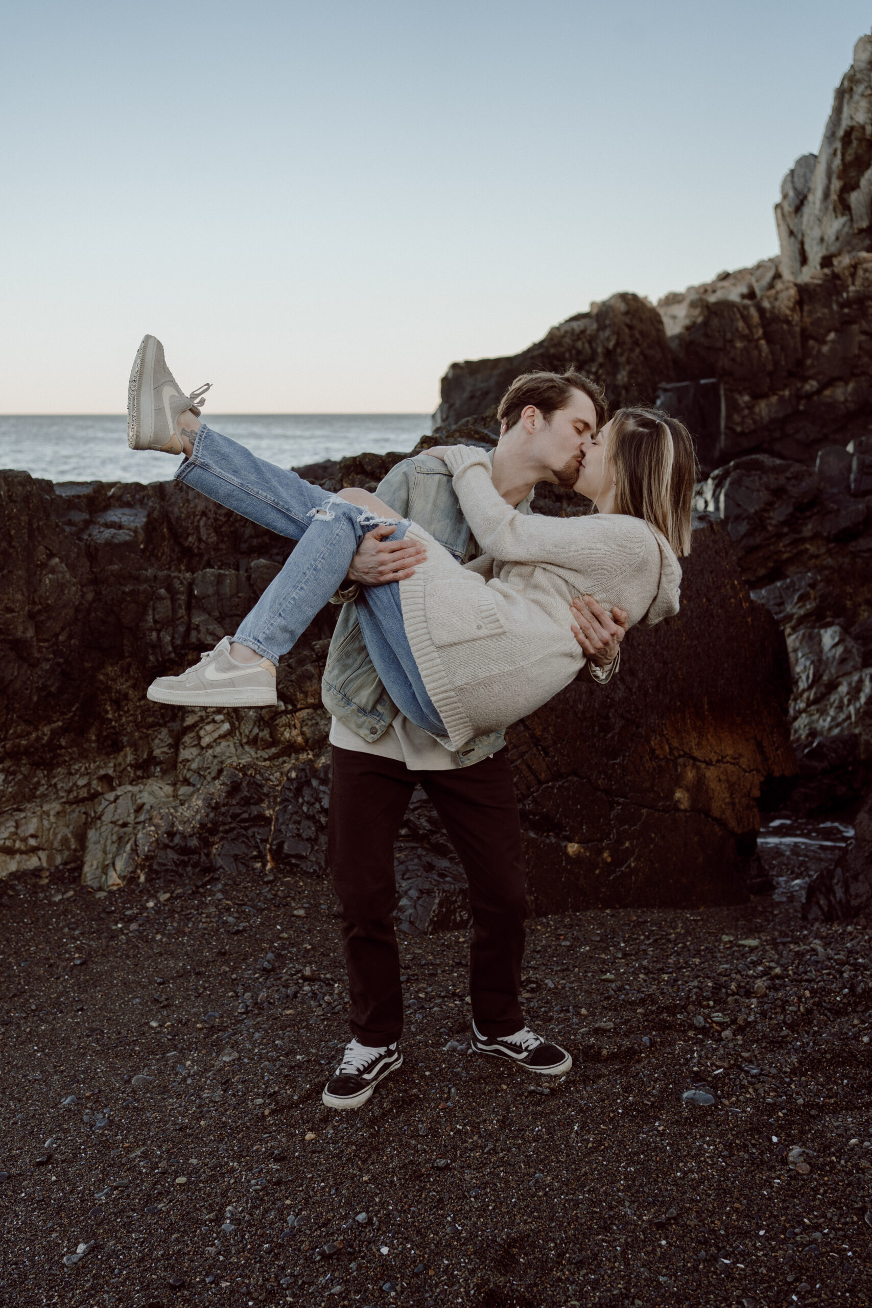 Engagement photo session at Castle Rock, Marblehead, MA: A couple embraces against the scenic backdrop of Castle Rock, with the fiancé tenderly dipping his partner into a kiss, capturing their love and joy