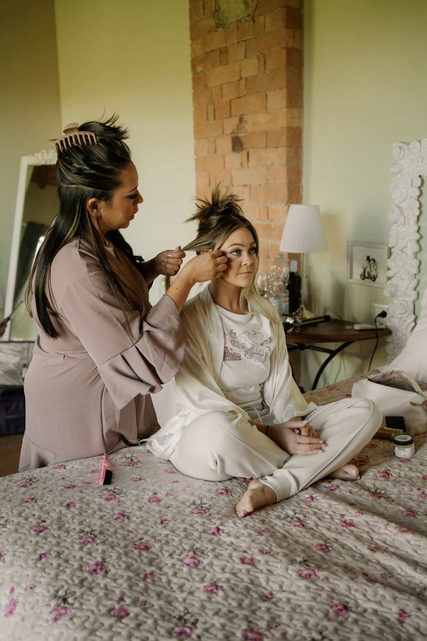 Bride getting ready in her pjs with one of her bridemaids doing her hair