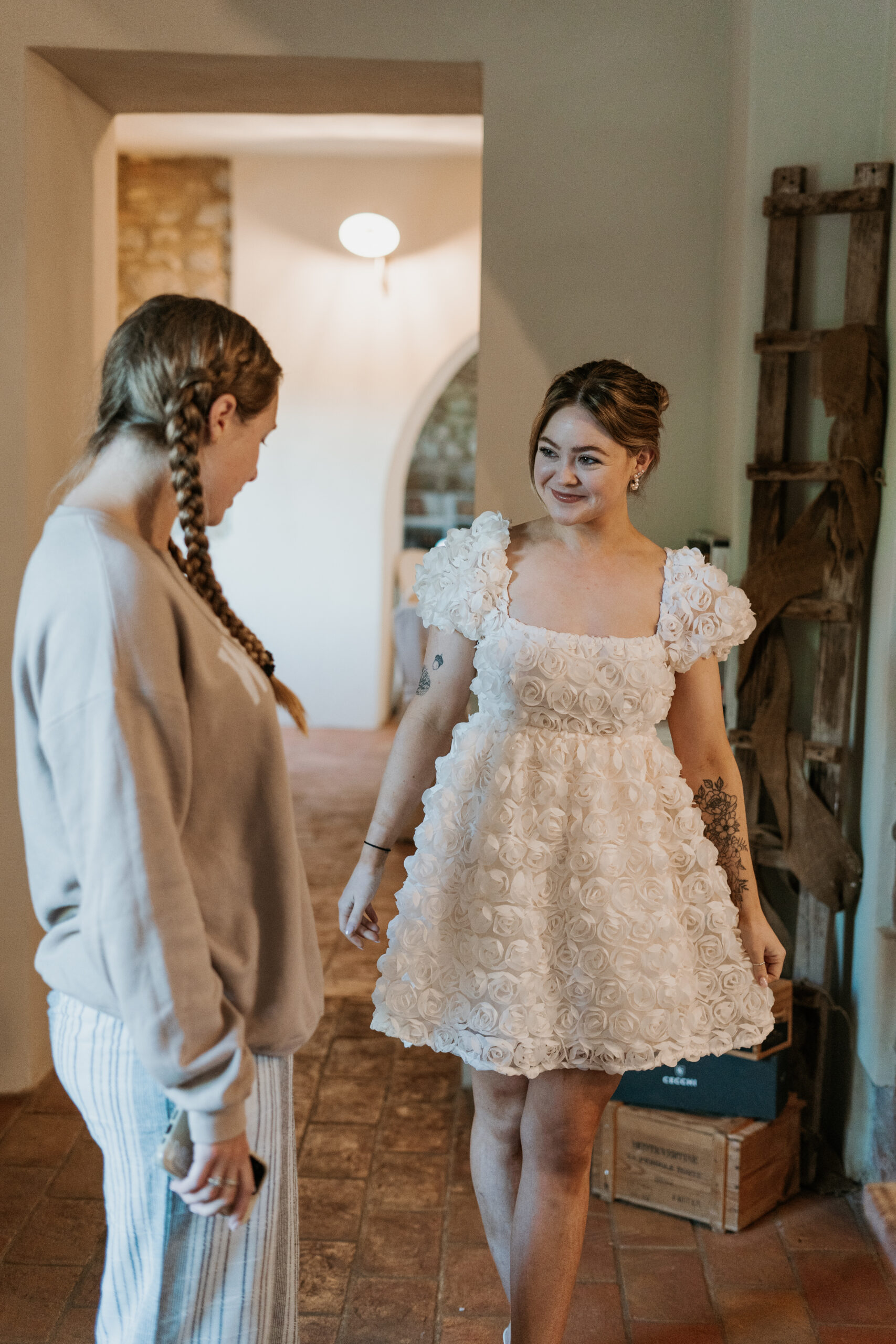Bride, wearing a white rose bud cocktail dress, shows it off to her Maid of Honor in the Italian Villa for the wedding brunch