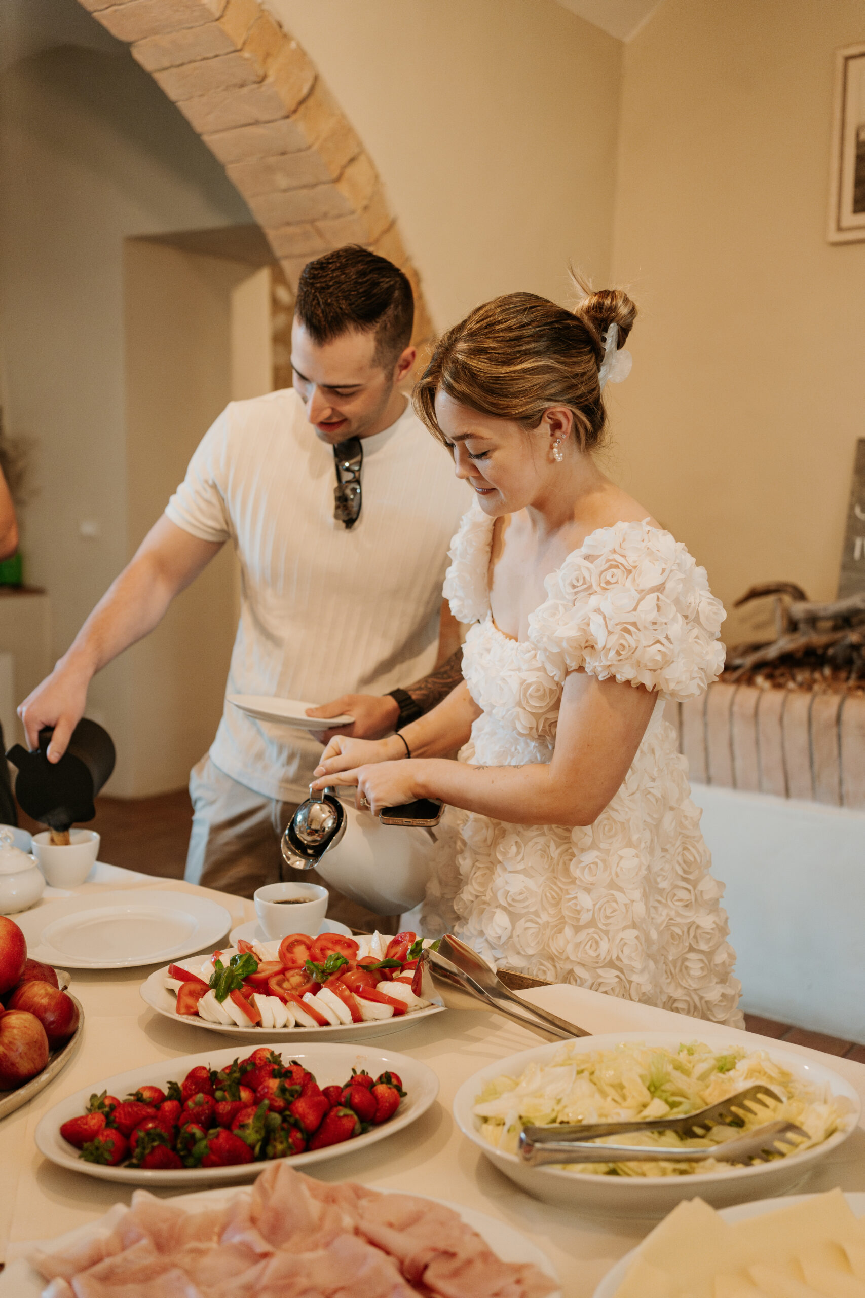 Bride, wearing a white rose bud cocktail dress, pours her morning coffee with her groom by her side during the bridal brunch in Tuscany