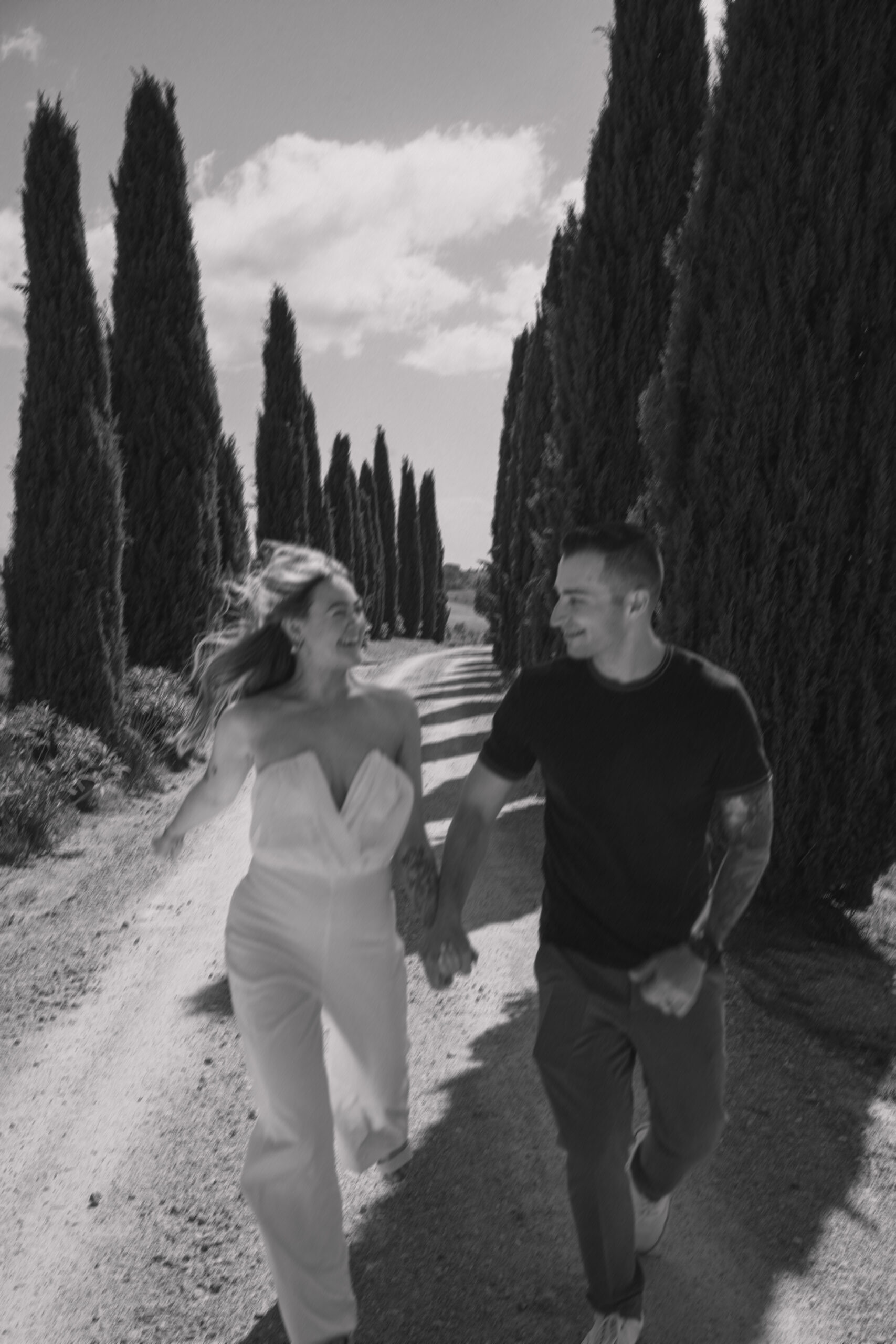 Bride and groom run romantically while looking at each other in the middle of rows of Tuscan Pines during their Italy destination wedding excursion