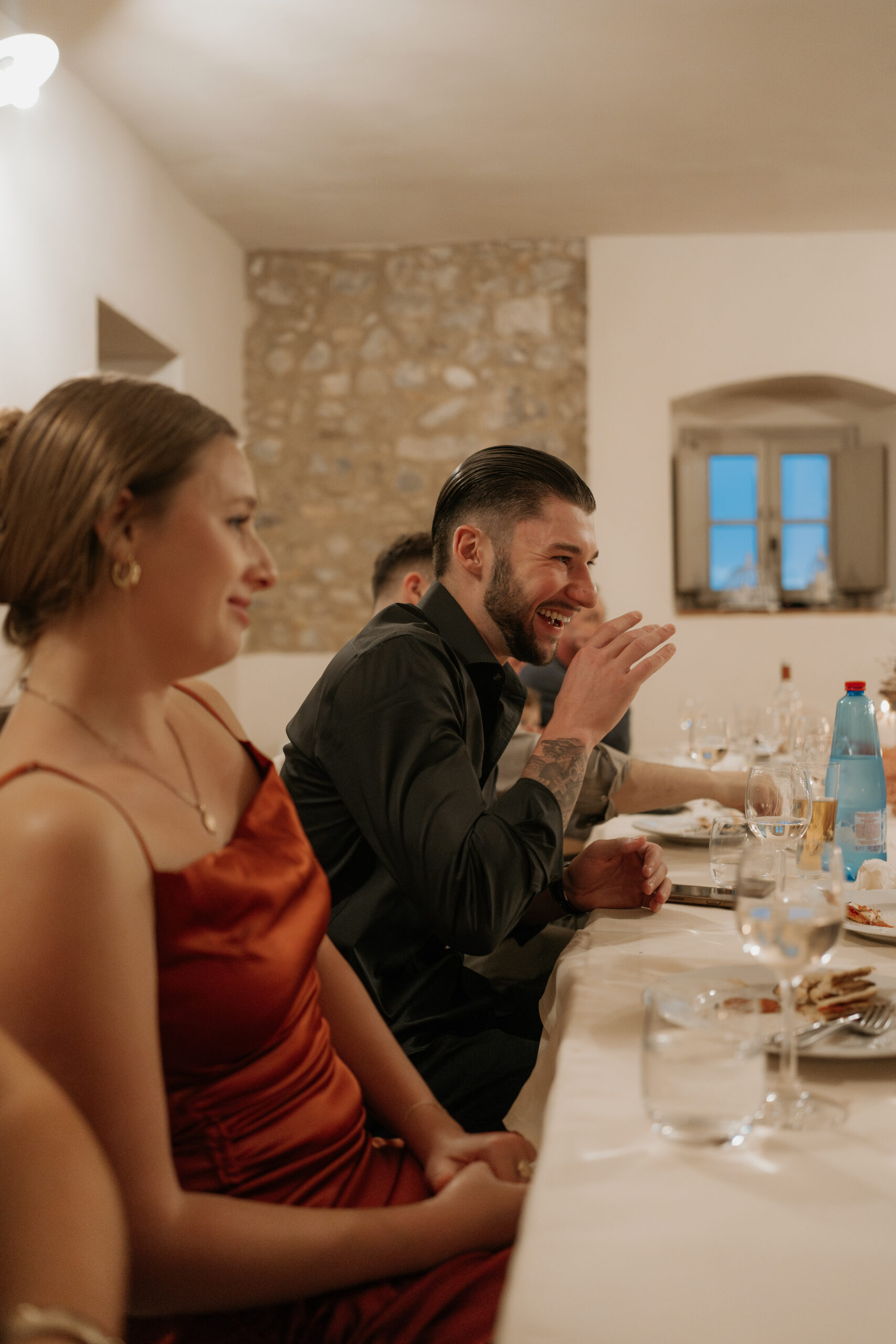 Best man laughs while at the table during the Tuscan destination wedding candle lit rehearsal dinner