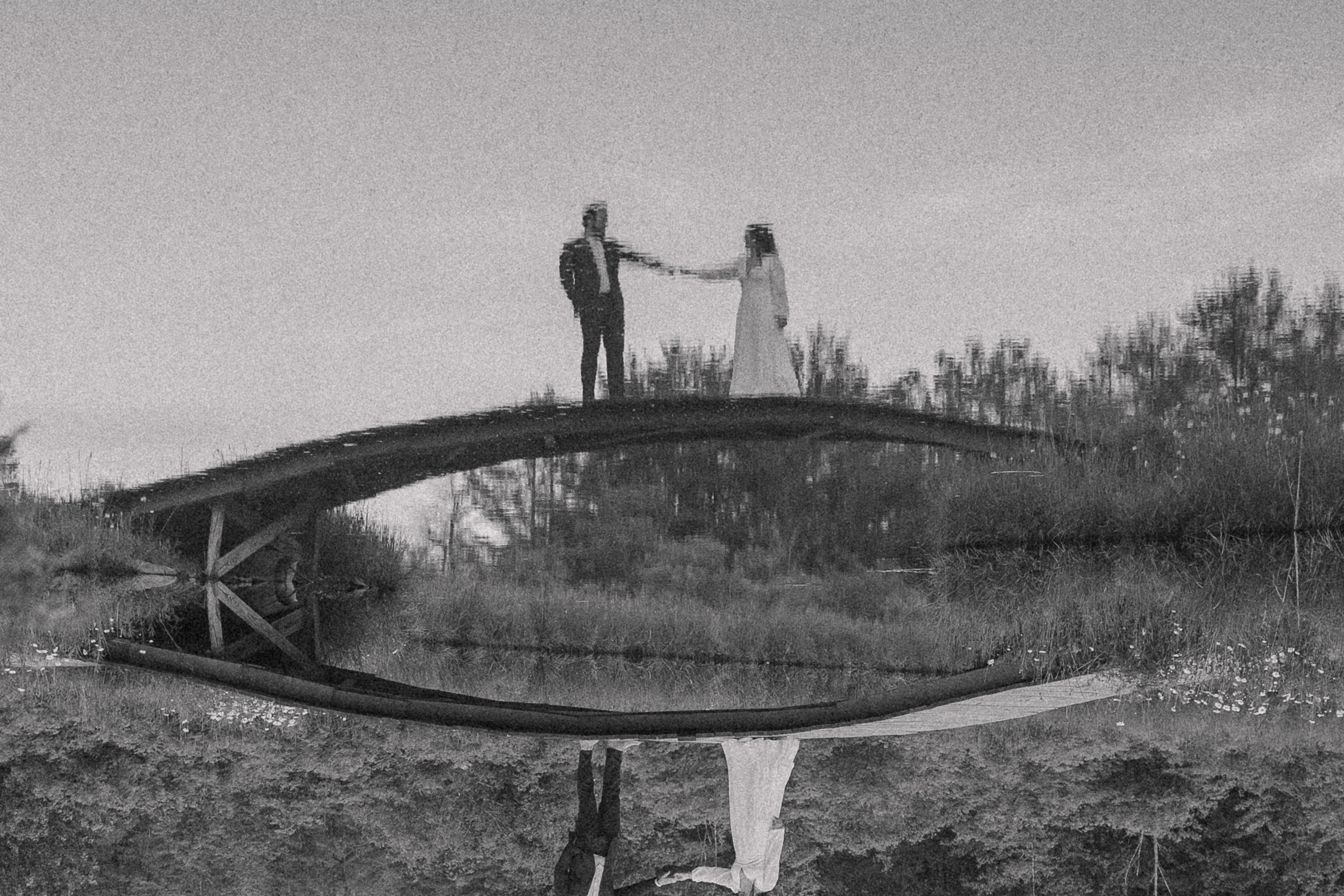 Artistic Bride & Groom Wedding Portrait on a bridge and you see the reflection of them holding hands in the water