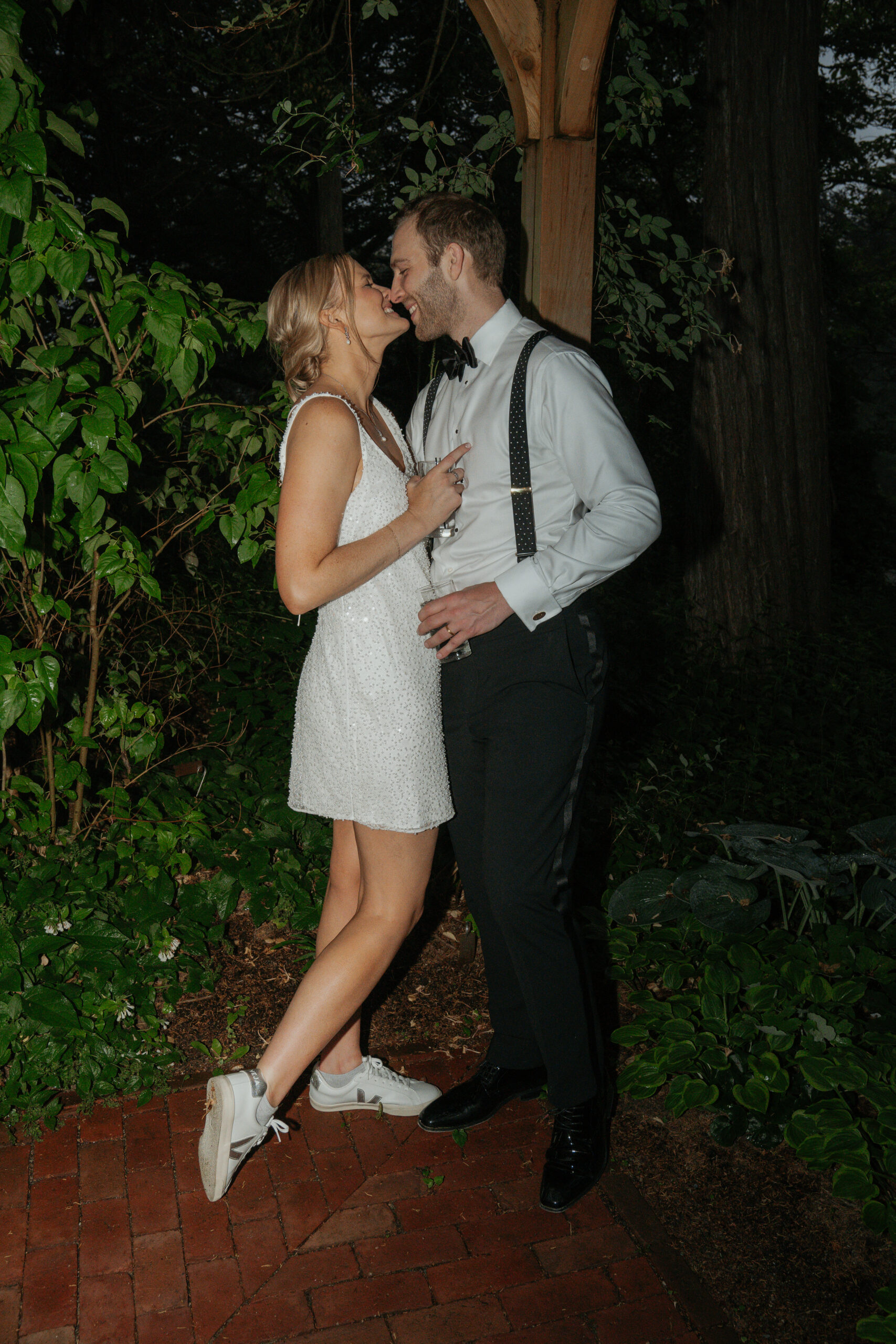 Bride and Groom leaning in for a kiss in their wedding reception party attire. They stepped away for a private moment at their summer garden party wedding.