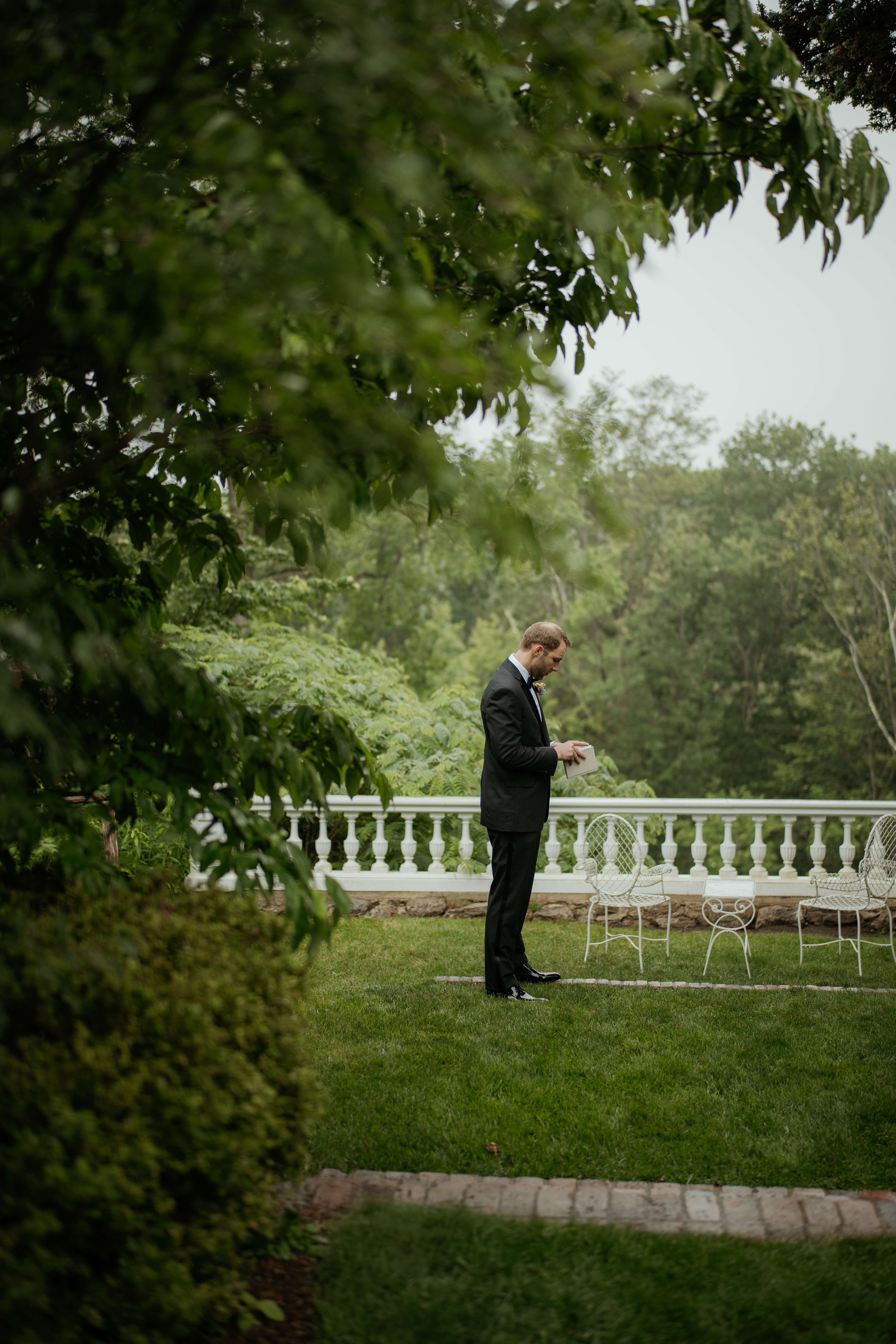 Groom reading over his wedding vows before his private first look with his bride to be. He is by the terrace at Long Hill in Bevery, MA surrounded by greenery.