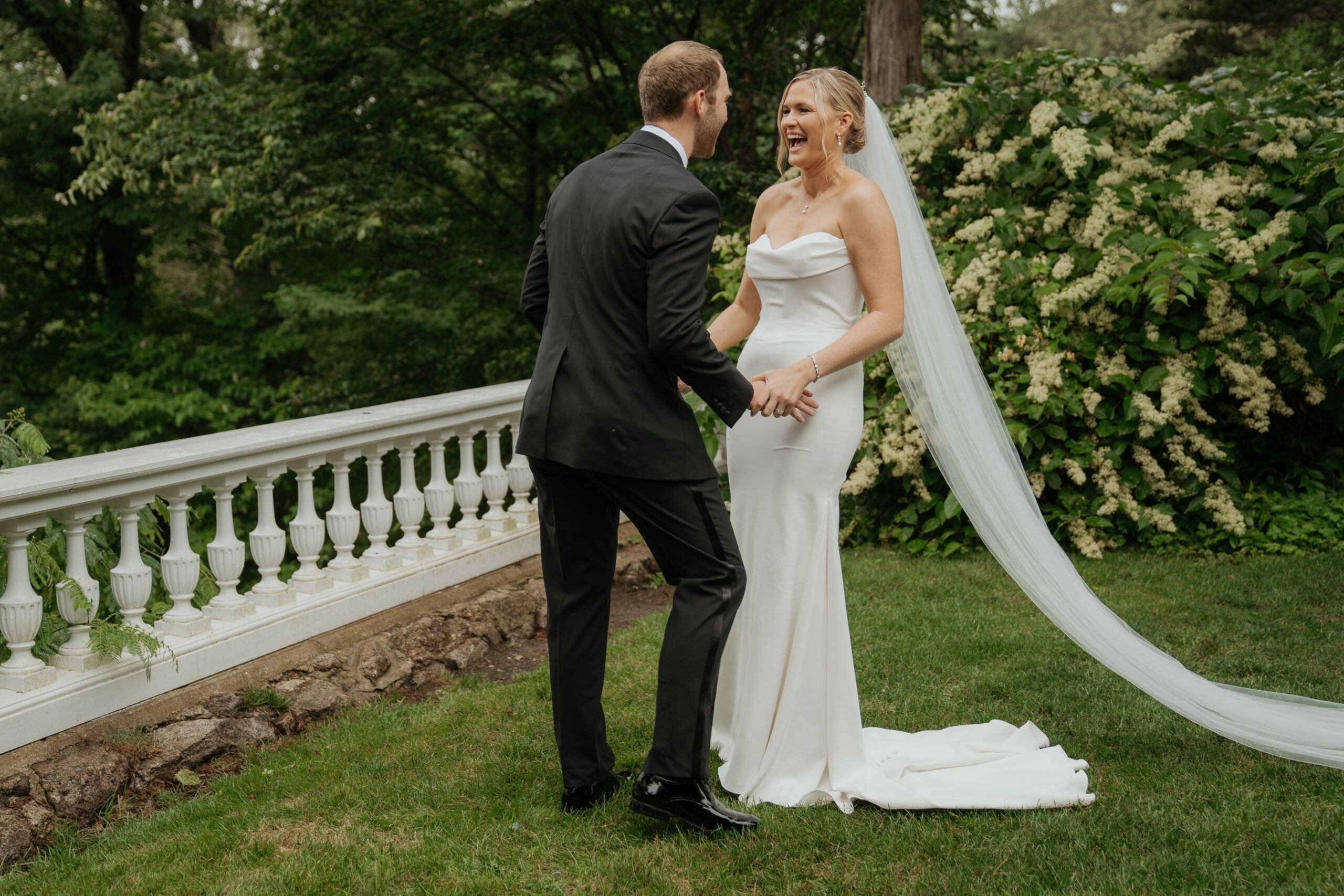 Bride and groom share a laugh as they're holding hands in their wedding attire. 