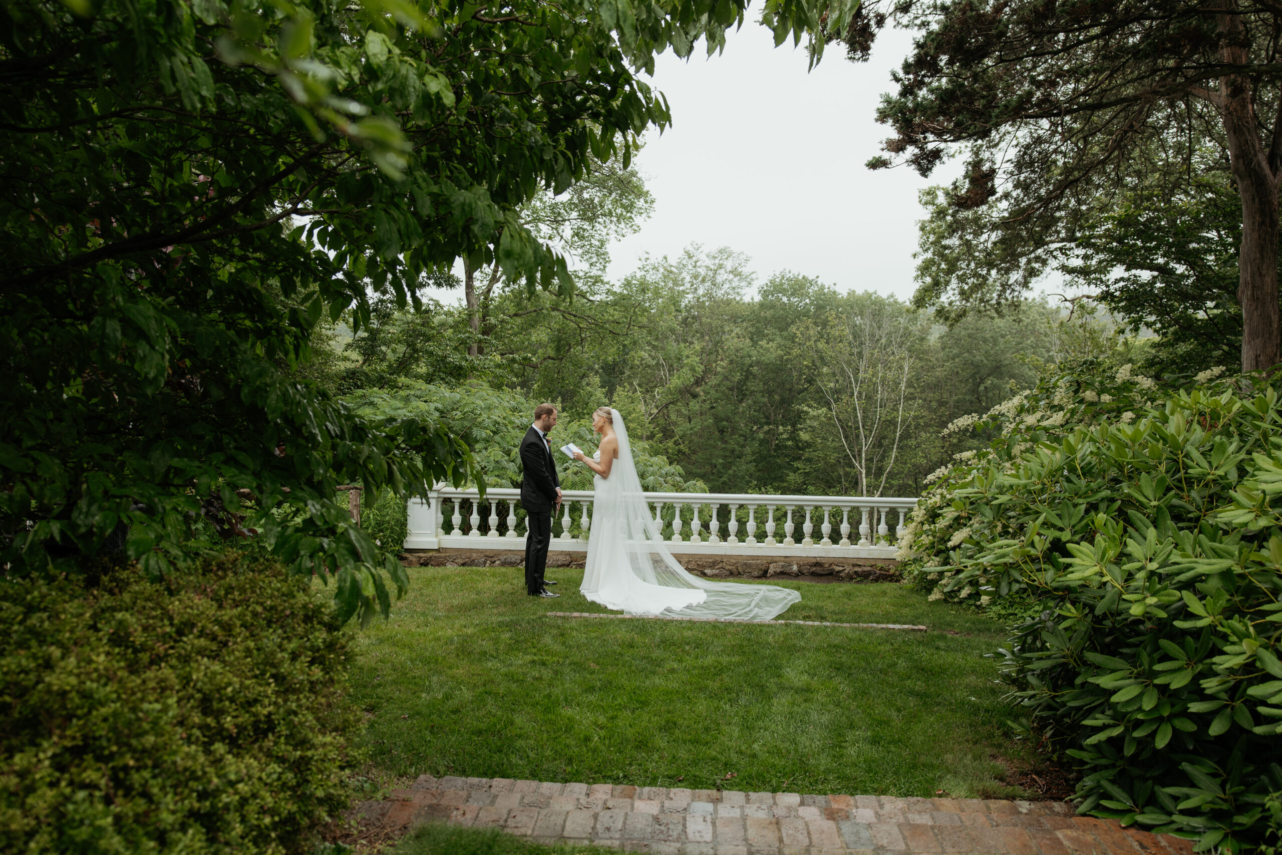 Bride and groom sharing their private vows along the terrace at Long Hill in Beverly, MA. They are framed with luscious greenery as they share this intimate and intentional moment, just the two of them.