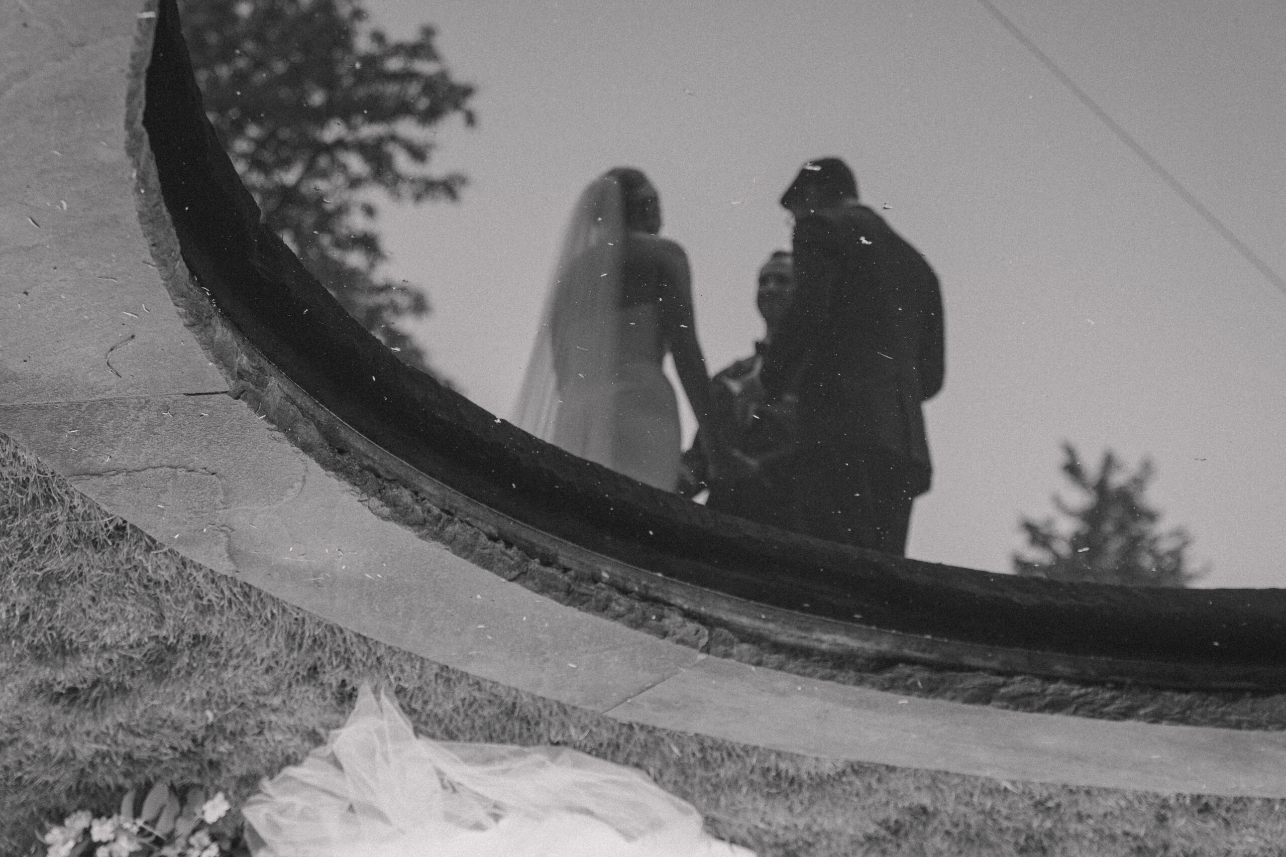 reflection of bride and groom in a fountain as they are exchanging vows at their summer garden party wedding ceremony at Long Hill in Beverly, Massachusetts.
