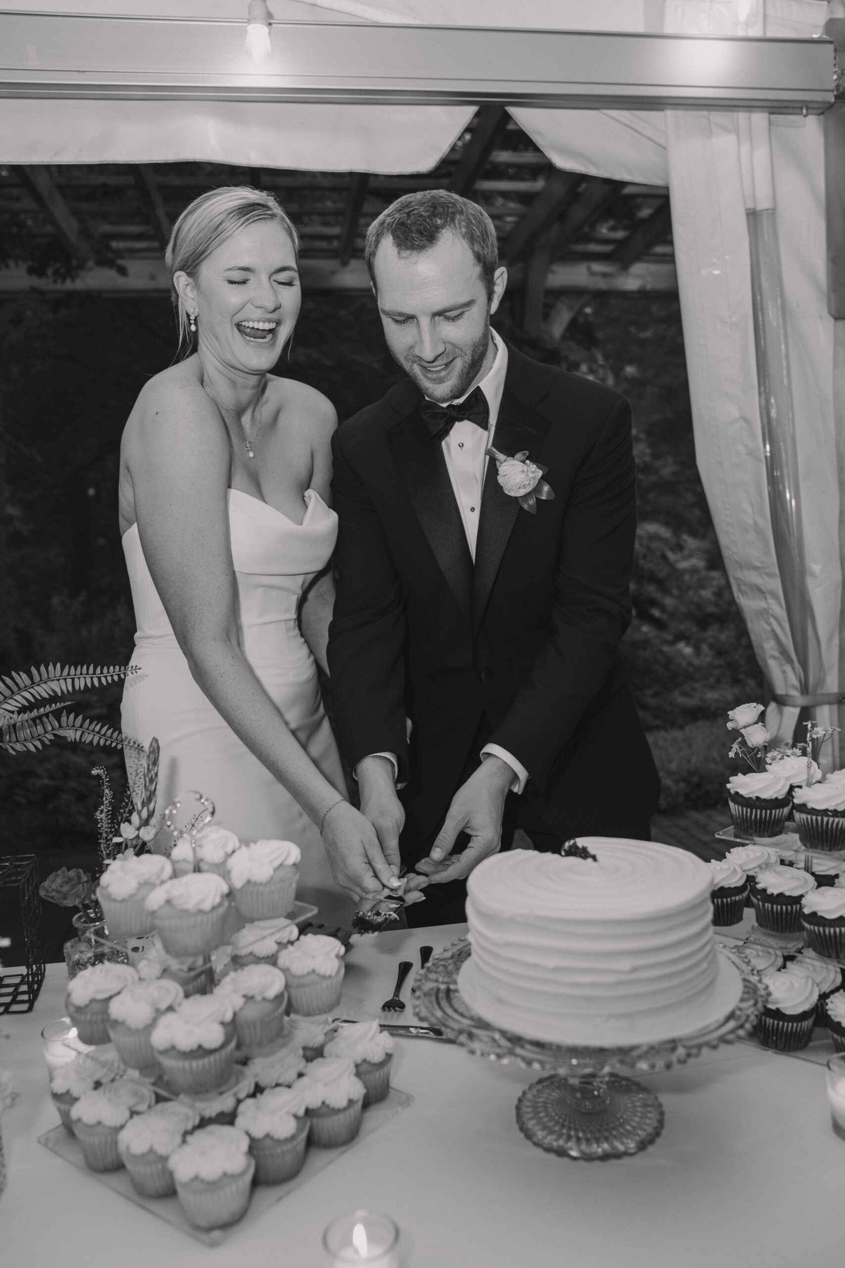 Bride & groom laughing as they are cutting their simple wedding cake at their summer garden party wedding in New England.