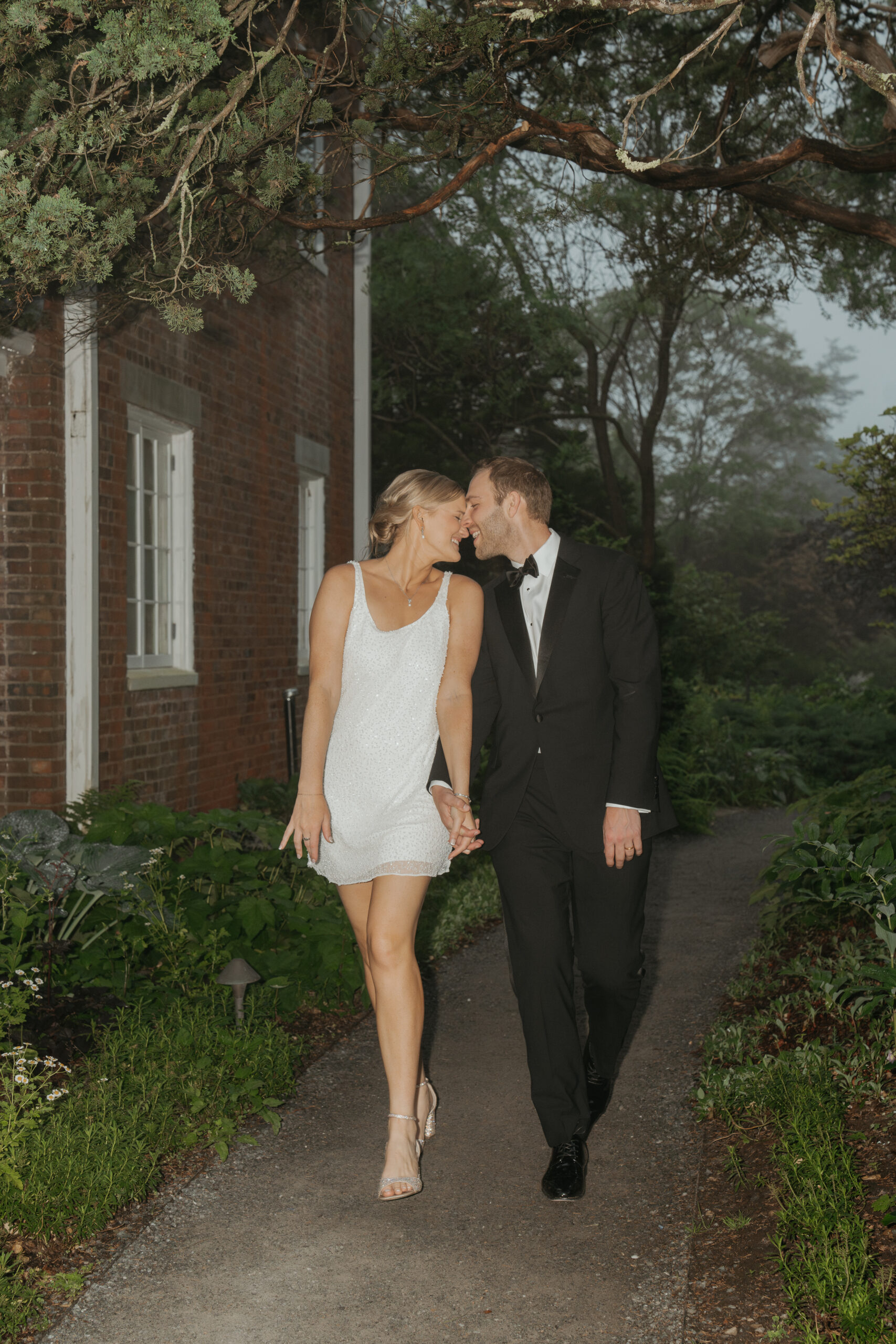 Bride and groom pressing foreheads together as they are holding hands and walking into their summer garden party wedding reception. They are in their wedding reception party attire