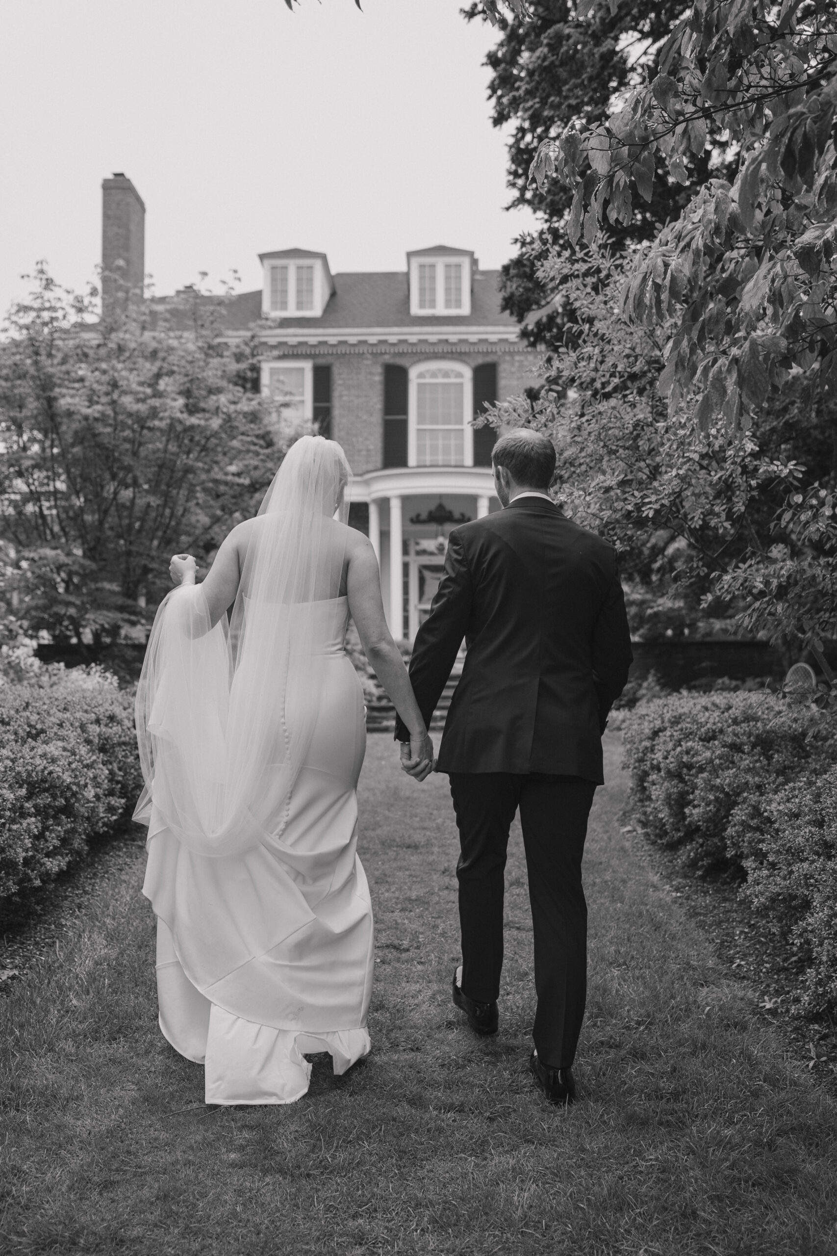 Bride and groom holding hands walking towards the mansion facade of Long Hill after their first look