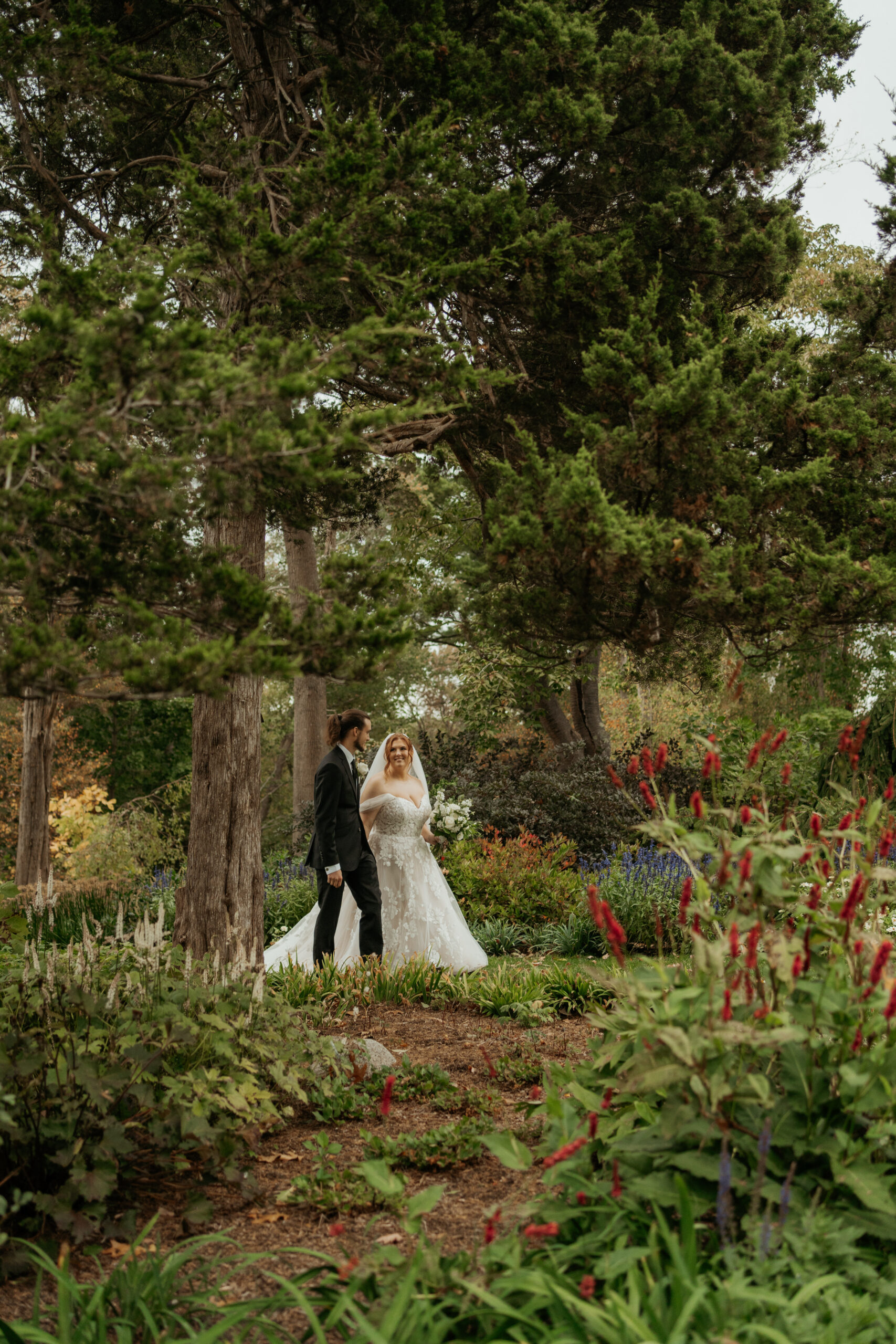 Bride and groom looking at each other and walking hand in hand through the colorful layered gardens on Long Hill wedding venue
