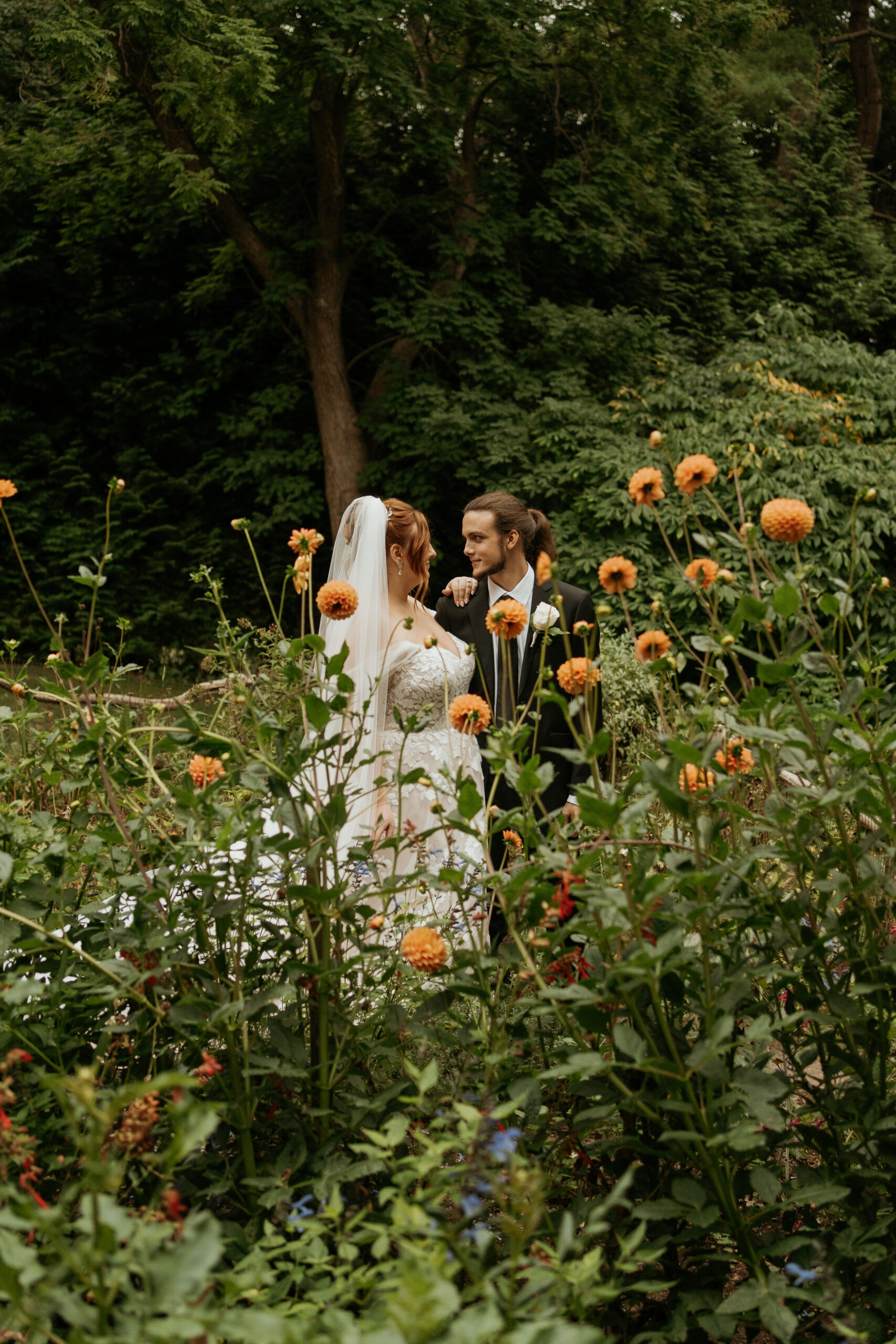 Bride and groom look at each other fondly surrounded by orange flowers in the gardens of Long Hill