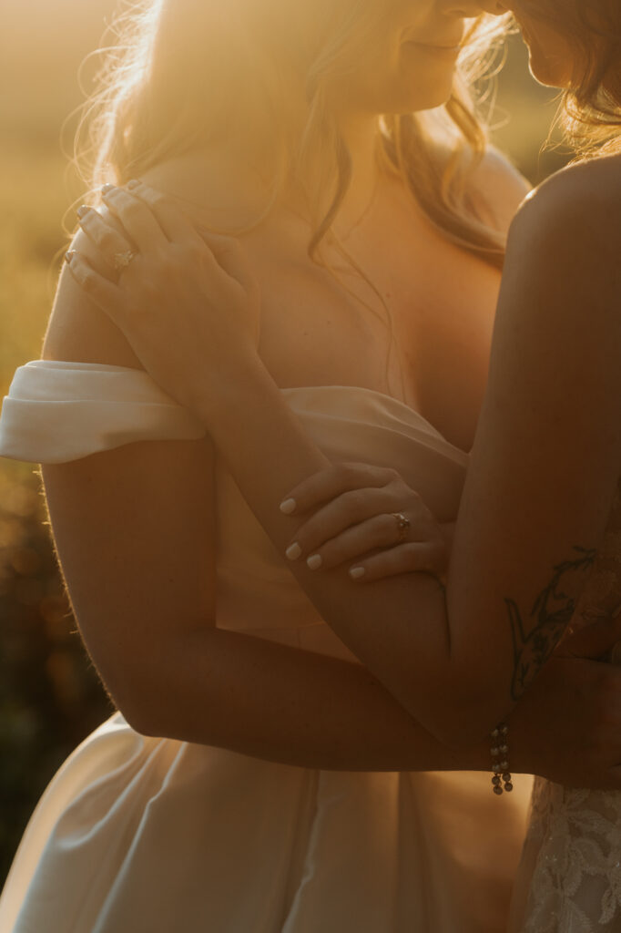 Golden hour close up wedding portrait of two brides embracing. Both wedding rings are being highlighted.