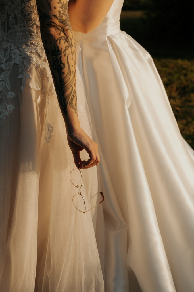 Second photographer perspective of the same moment, except it is from behind the brides. one bride is delicately holding her glasses in the golden light.